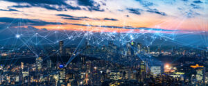 Aerial view of a city at dusk with glowing digital network lines connecting buildings against a colorful sky.