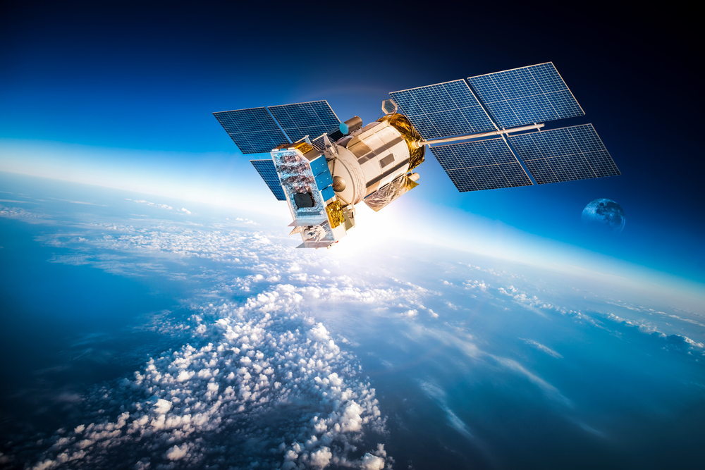 A satellite orbiting Earth above clouds with distant moon visible in the background.