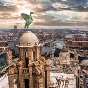 Rooftop view of a city with a prominent winged statue, historic buildings, and a sunset sky.