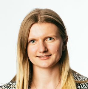 Person with long blonde hair, smiling, wearing a patterned top against a plain white background.