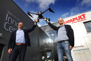 Two men holding a drone outside the Westcott Innovation Centre and Catapult Satellite Applications building.