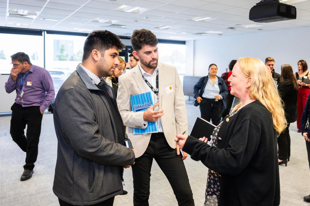 People in formal attire engaged in conversation at a professional event in a conference room.