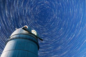 Time-lapse photo of star trails forming circles in the night sky above an observatory telescope.