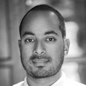 Black and white portrait of a man with short hair and a trimmed beard, looking directly at the camera.