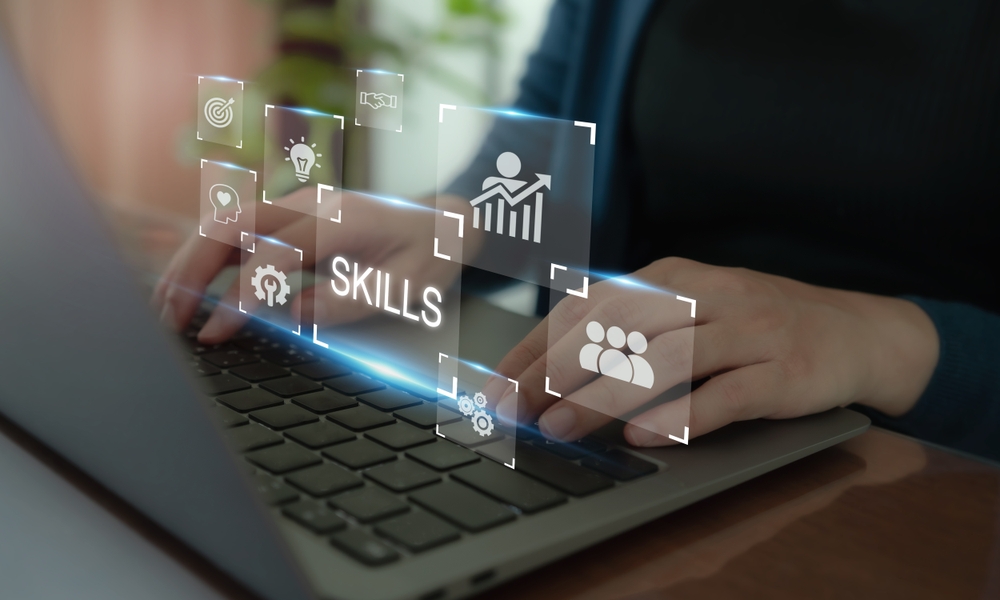 Hands typing on a laptop with virtual icons representing skills and professional growth floating above the keyboard.