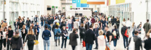 Large crowd of people walking through a bright, spacious convention center or hallway.