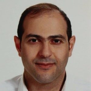 Portrait of a man with short dark hair, wearing a white collared shirt, against a plain background.