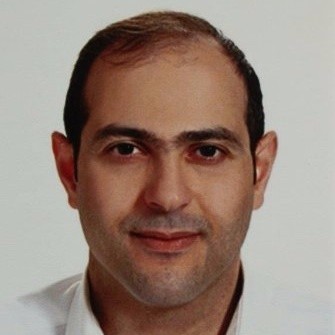 Portrait of a man with short dark hair, wearing a white collared shirt, against a plain background.
