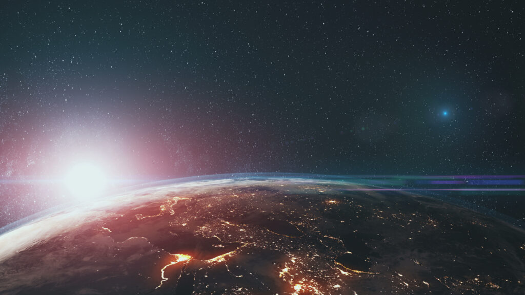 View of Earth from space with the sun rising over the horizon, showing city lights and a star-filled sky.