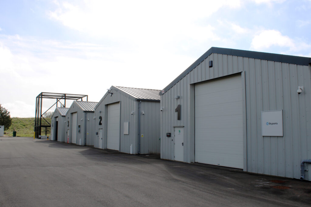 Three grey industrial warehouse buildings labeled 1, 2, and 3 with large garage doors and a paved lot.