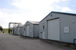 Three grey industrial warehouse buildings labeled 1, 2, and 3 with large garage doors and a paved lot.