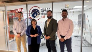 Four people stand in front of Space Enterprise Lab and IDEALondon office windows, posing for a group photo.