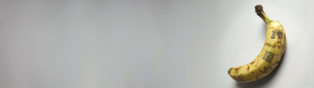 A ripe banana with QR codes printed on its peel, placed against a plain light background.