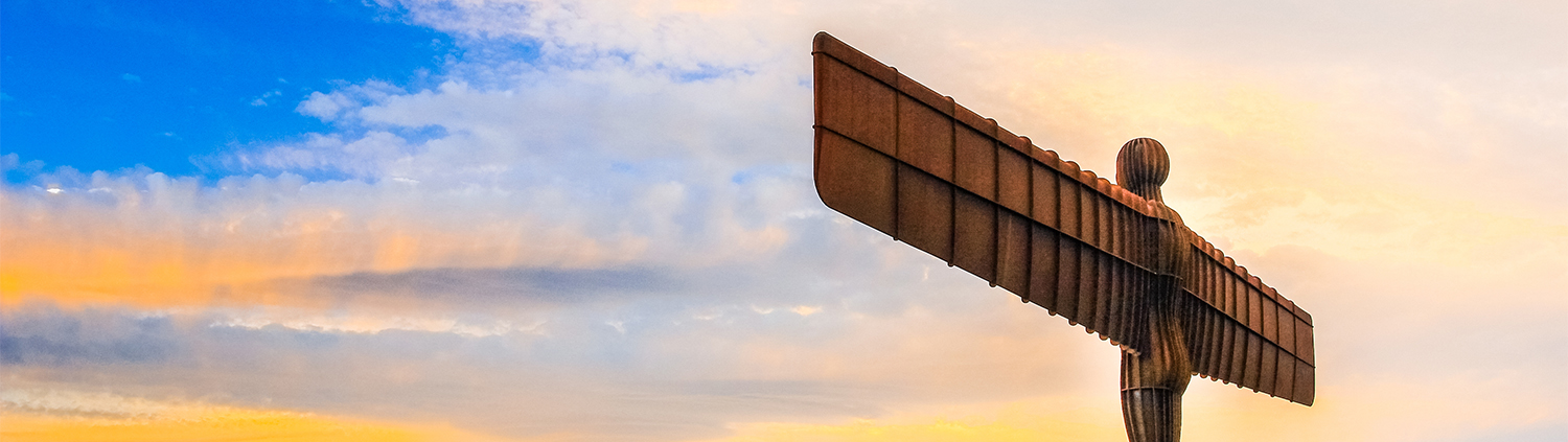 The Angel of the North sculpture stands against a colorful sunset sky with blue, orange, and yellow clouds.