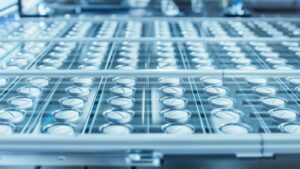 A close-up of rows of empty glass vials on a production line in a pharmaceutical factory.