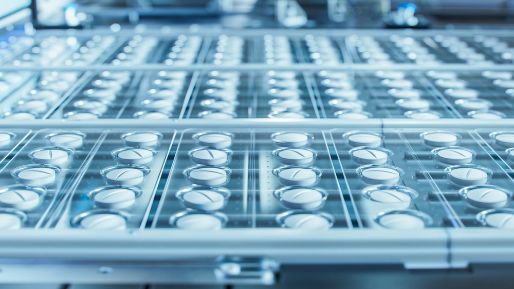 A close-up of rows of empty glass vials on a production line in a pharmaceutical factory.