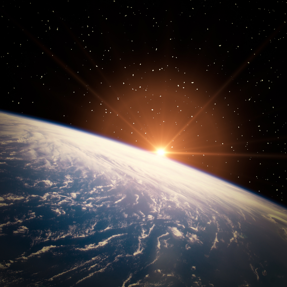 Sunrise over Earth’s horizon seen from space with a starry sky in the background.