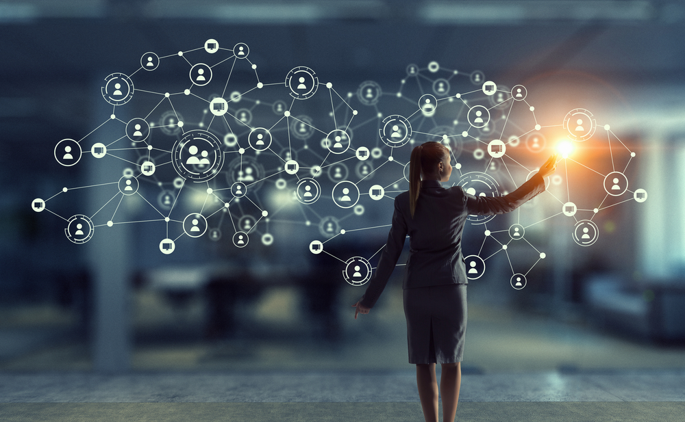 Businesswoman touches a glowing digital network of connected people icons in a modern office setting.