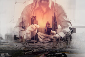 Double exposure of a man using a smartphone overlaid with a cityscape and tall modern buildings.