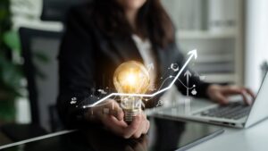 A businesswoman holds a glowing lightbulb with rising graph icons, symbolizing innovation and growth.
