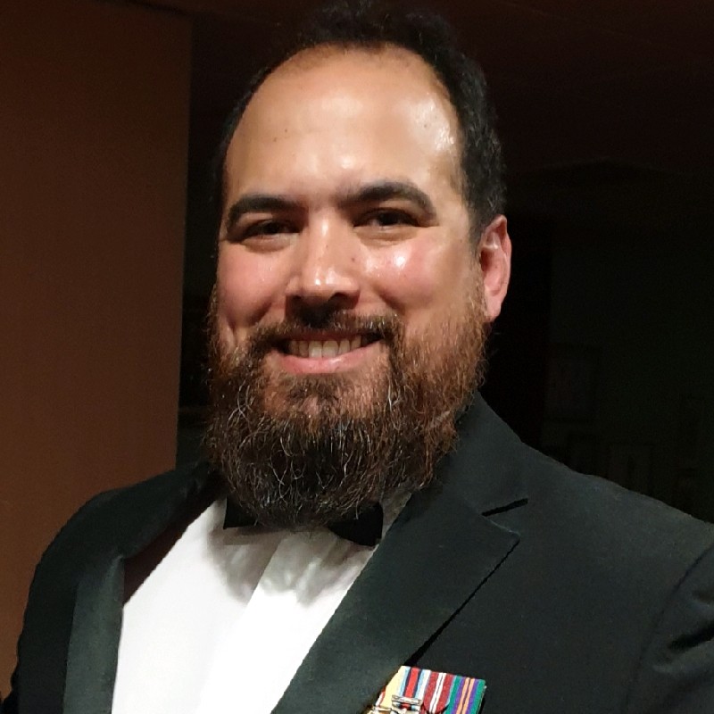 Smiling man with a beard in a tuxedo and bow tie, wearing military ribbons on his jacket.