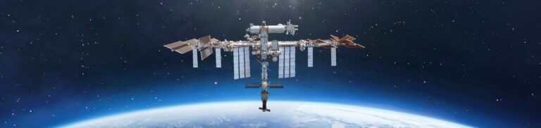 The International Space Station orbits above Earth with a backdrop of stars and the planet's horizon below.