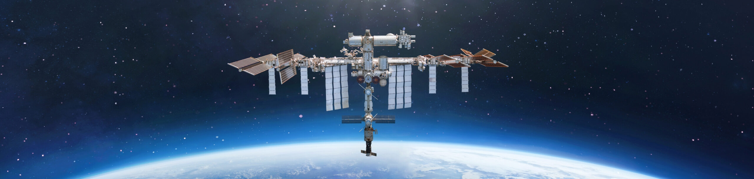 The International Space Station orbits above Earth with a backdrop of stars and the planet's horizon below.