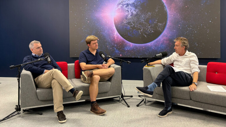 Three men sitting in armchairs during a podcast recording in front of a digital screen showing Earth.
